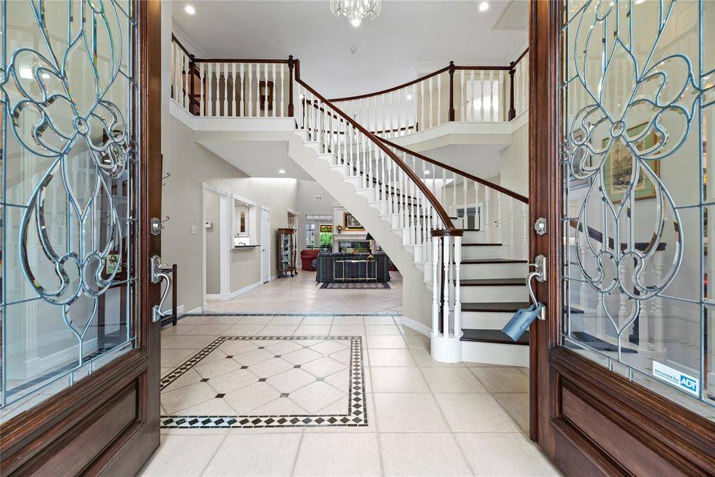 Welcoming entrance with elegant double 8' front doors with decorative glass, opening into a bright foyer. The space leads gracefully to the curved front staircase and offers a preview of the home’s open and inviting layout beyond.