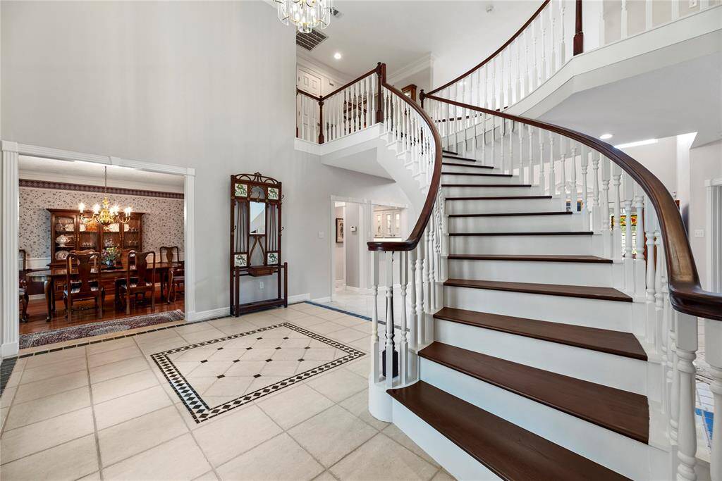 The entryway features a grand curved staircase leading to the upper level. The spacious foyer has tiled flooring with a decorative inlay, and opens to a formal dining room.