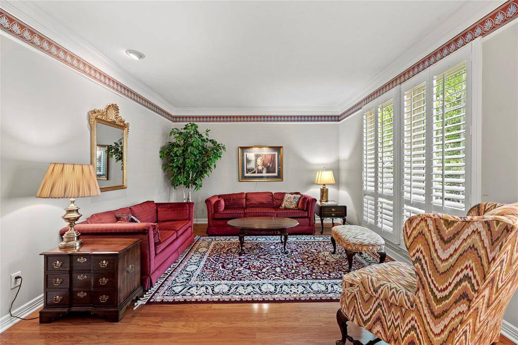 The living room, located at the front of the home, features rich wooden floors and large windows with classic shutters that fill the space with natural light, creating a warm and inviting atmosphere.