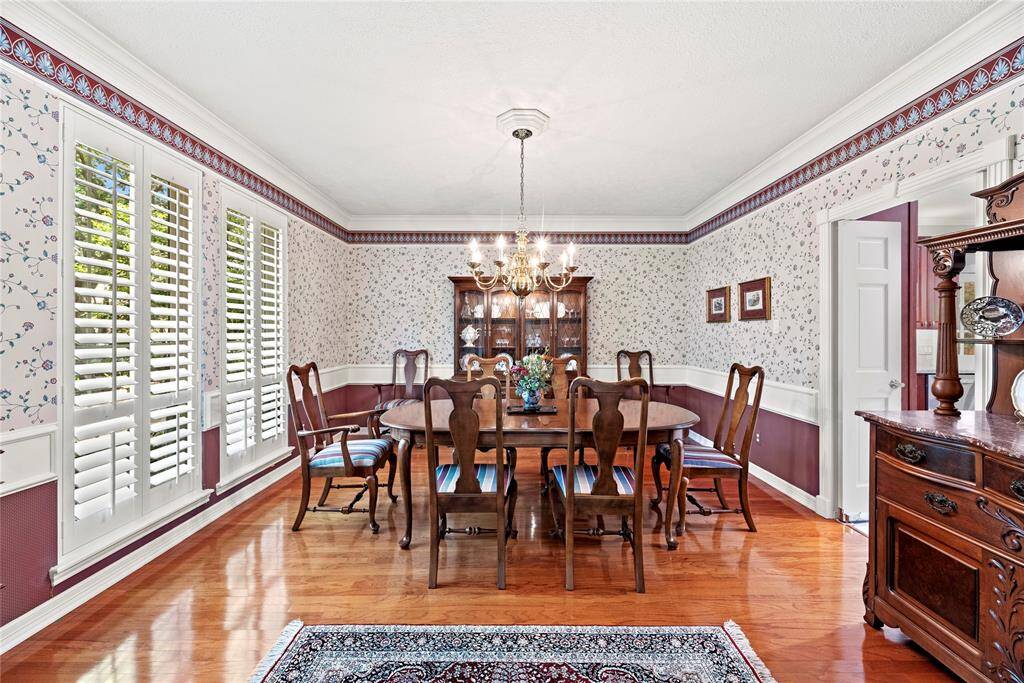 The formal dining room, with views of the professionally landscaped front yard, features a stylish chandelier, and rich wood flooring, with lots of natural light streaming through plantation shutters.