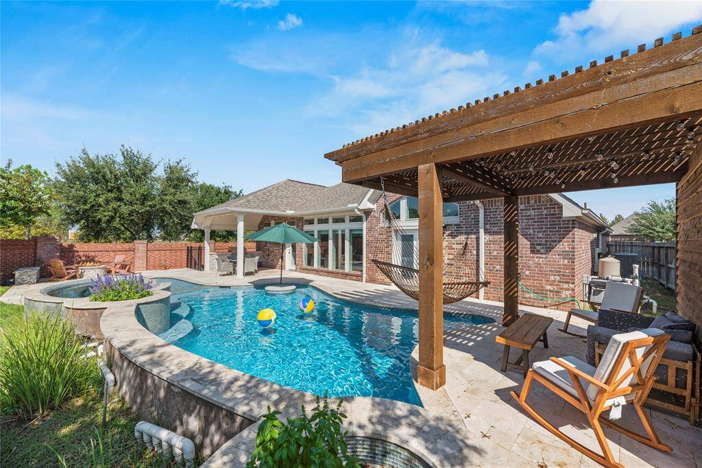 This backyard oasis features a sparkling pool with a spa, a wooden pergola with a hammock, and ample seating. Perfect for relaxation and entertaining, it offers a blend of comfort and luxury.
