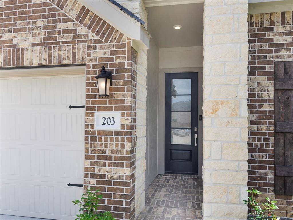 Charming brick and stone entryway with a modern black door, stylish outdoor lighting, and a covered porch. The home has an inviting curb appeal with a neatly numbered address.
