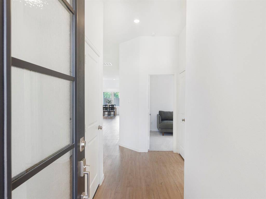 This photo shows a bright entryway with high ceilings, light vinyl flooring and white walls. It leads into an open living area with natural light.