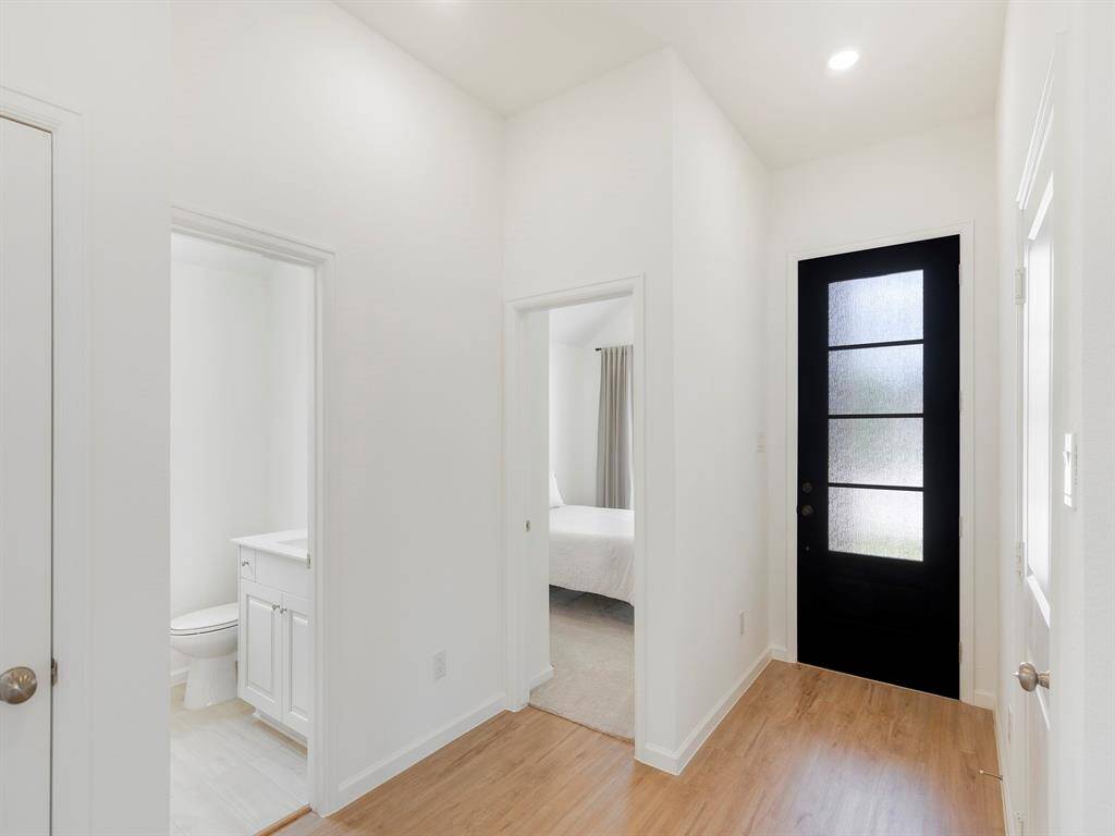 This photo shows a bright, modern entryway with light vinyl flooring and modern white walls. It features a sleek black front door with frosted glass panels.