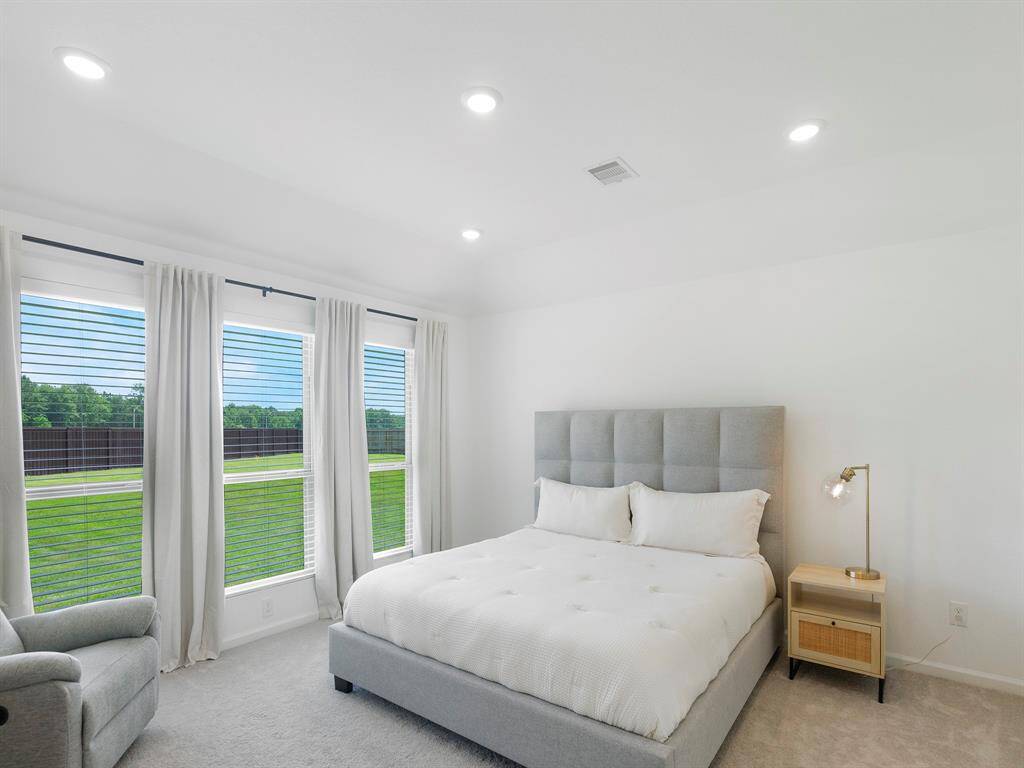 The serene primary bedroom offers comfort and space, featuring soft wall-to-wall carpeting that adds warmth underfoot. High tray ceiling enhances the airy atmosphere, while three generously sized windows line one wall, inviting in natural light and creating a bright, open retreat.