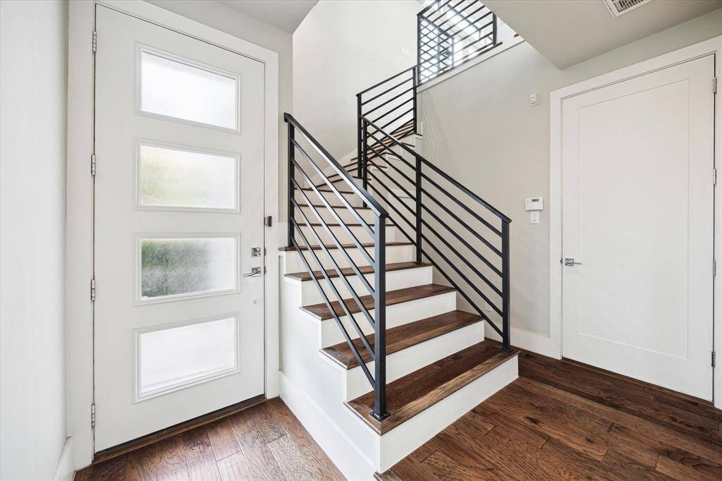 A spacious and bright entryway, boasting a modern staircase. You will find ample storage space, under the stairs and in a coat closet to the right of this photo. The door to the right leads to a 2 car garage with epoxy flooring.