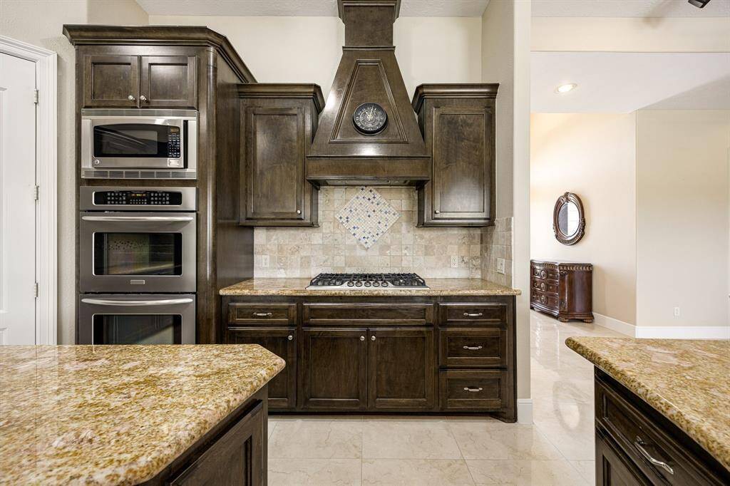 A double oven and built-in microwave are thoughtfully positioned next to the gas range with a custom vent hood, creating a chef-friendly layout. Rich wood cabinetry and a spacious walk-in pantry provide abundant storage for all your kitchen essentials.