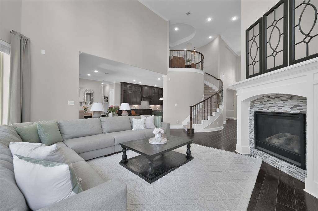 Spacious living room with high ceilings and elegant design. Features include a cozy fireplace, a stylish open staircase and provides an open floor plan for entertaining. This open layout connects to a modern kitchen, creating a welcoming and airy atmosphere.