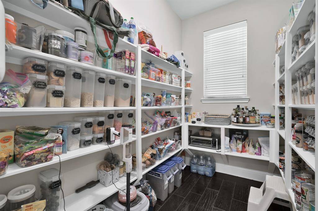 This photo showcases a spacious walk-in pantry with multiple shelves.  It features a window for natural light and wood flooring, providing a clean and efficient storage space.