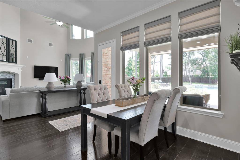 This bright, open-concept living and dining area features high ceilings, large windows with views of the backyard, and elegant hardwood floors. The space boasts a beautiful gaslog fireplace, offering a warm and inviting atmosphere.