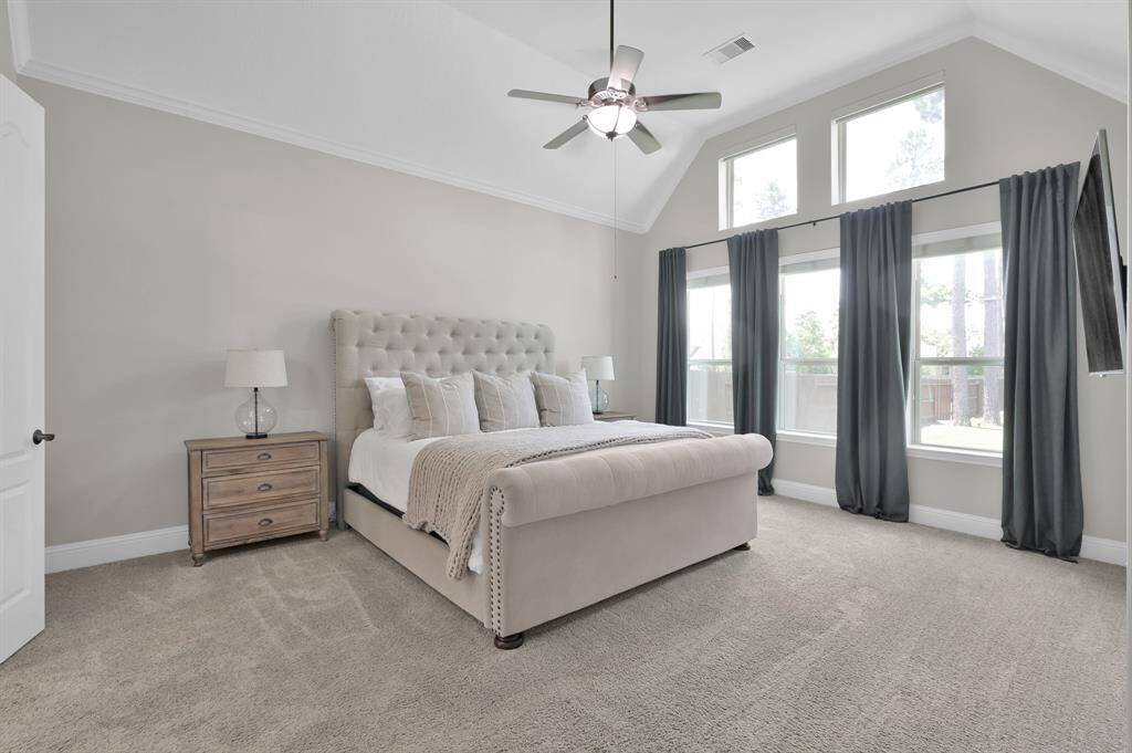 This spacious Owner's Retreat bedroom features a vaulted ceiling with ceiling fan, large windows with abundant natural light, and neutral-toned walls. The upper windows include custom shades operated remotely to extend your privacy or allow for star gazing.