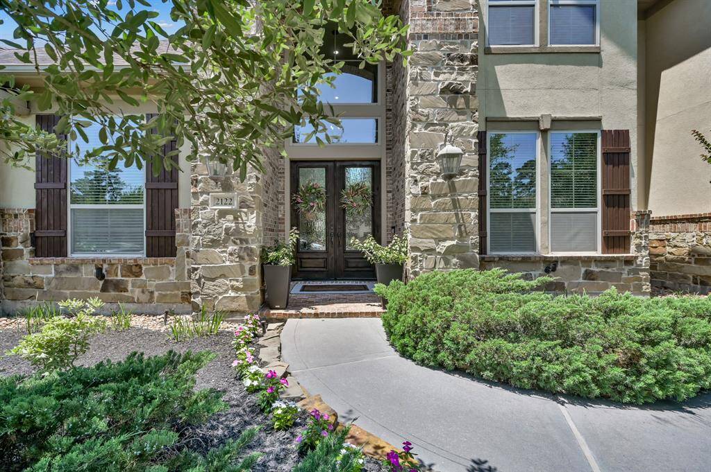 Charming two-story home with a well-maintained front yard, spacious driveway, and five-car garage. The exterior features a mix of stone, brick and stucco, with mature trees and lush landscaping.