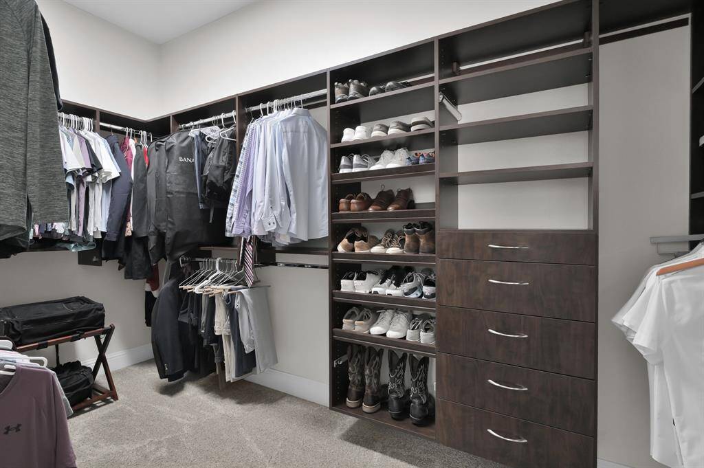 This image showcases a spacious walk-in closet with ample shelving, drawers, and hanging space, ideal for organizing clothes and shoes. The dark wood finish adds a touch of elegance, enhancing the room's functionality and style.