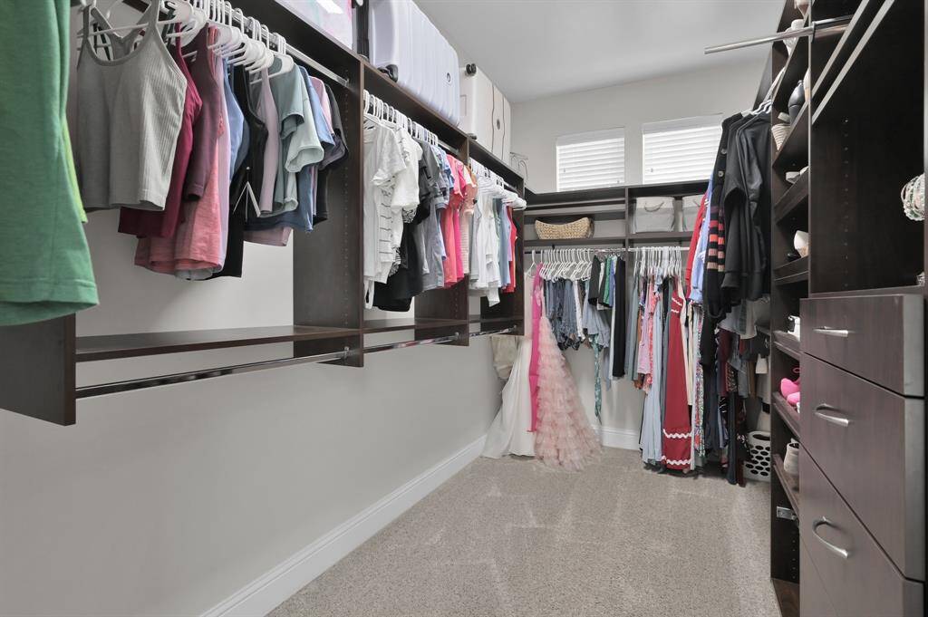 This spacious walk-in closet features dark wood shelving and drawers, ample hanging space, and natural light from two high windows, providing a well-organized and bright storage solution.