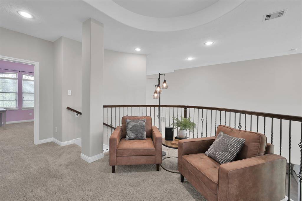 This photo showcases a cozy upstairs landing that provide a comfortable sitting area adjacent to the Game Room. The space features neutral walls, carpeted flooring, and a stylish railing, leading to a room with large windows. Perfect for a reading nook or relaxation area.