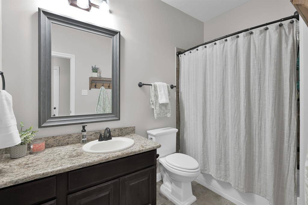 This bathroom features a granite-topped vanity with a modern dark wood cabinet, a large framed mirror, and a sleek sink. It has a shower-tub combination and is located just off one of the secondary bedrooms.  It is also conveniently near the Game Room and Media Room.