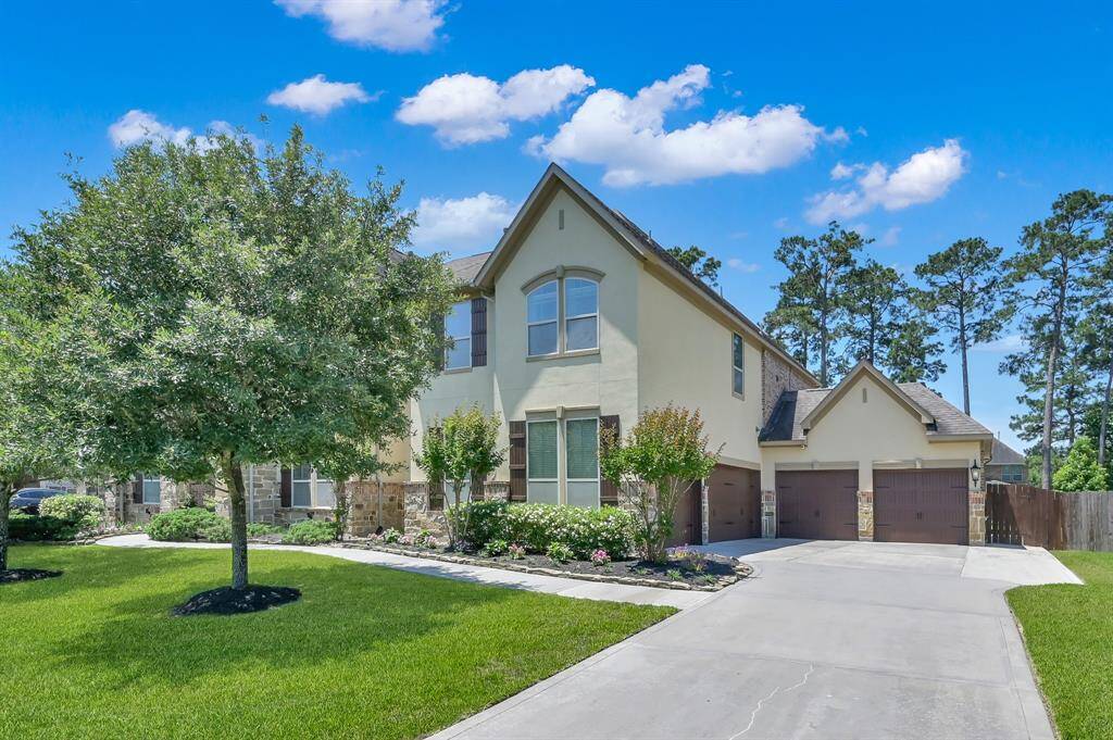 This photo showcases the front entrance of a modern, yet traditional home featuring a stone facade, elegant double doors, and well-maintained landscaping with shrubs and flowers, creating an inviting and charming curb appeal.