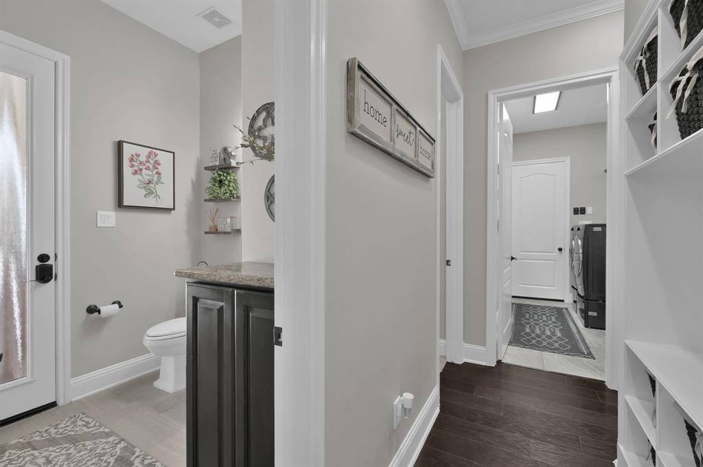 This photo showcases a hallway with a view of a half bathroom and a laundry room. The bathroom features a vanity, decor, and a door with frosted glass. The door leads directly out to the patio for easy access to the pool.