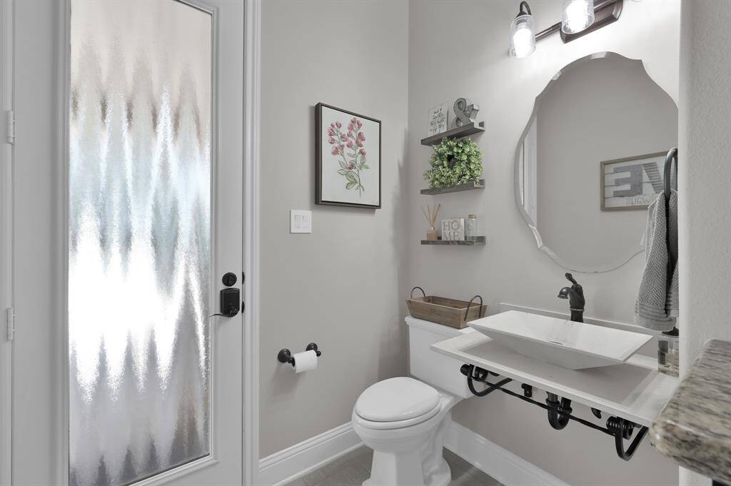 This photo shows a modern, spacious half bathroom with a stylish pedestal sink and a unique mirror. It features a frosted glass door for privacy, and leads directly outside to the pool area.