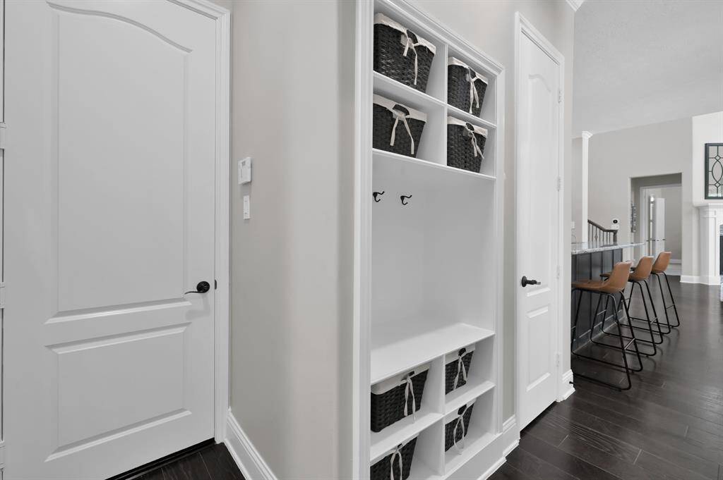 This photo showcases a modern hallway with built-in storage featuring shelves and hooks, perfect for organizing. The space leads into an open area with a sleek kitchen, breakfast room and the family living space.