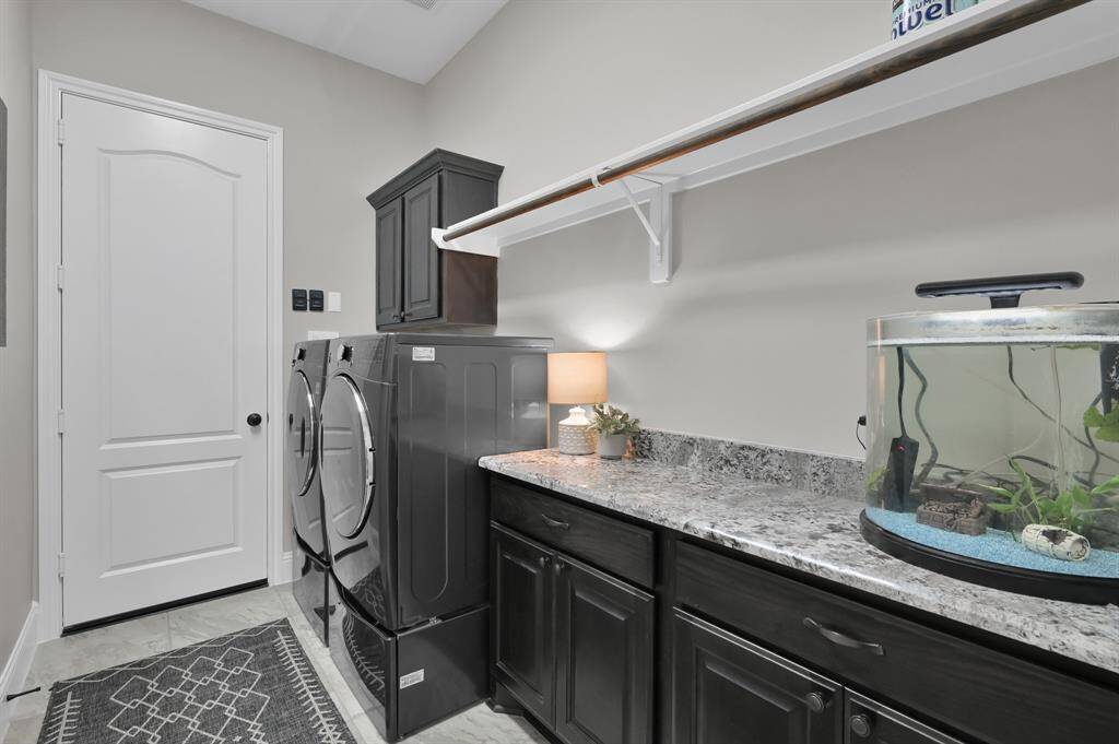 This laundry room features ample countertop space, and beautiful dark cabinetry. A shelf above provides additional storage, and the room is well-lit, creating a functional and stylish workspace.