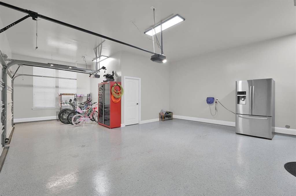 Spacious, well-lit garage with epoxy flooring, providing ample room for storage and parking. Features include a modern refrigerator, storage cabinet, and organized space for bicycles, making it ideal for both functionality and convenience.