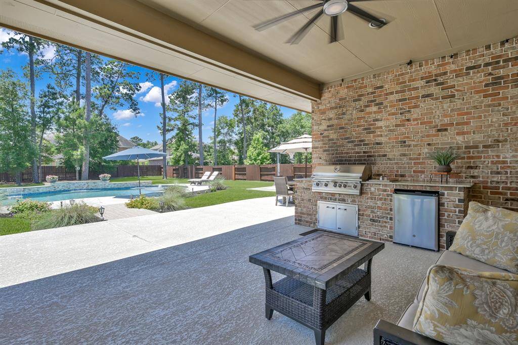 This photo showcases a spacious backyard with a covered patio featuring a ceiling fan, outdoor seating, and a built-in grill. The area overlooks a well-maintained pool and lush greenery, perfect for relaxation and entertainment.