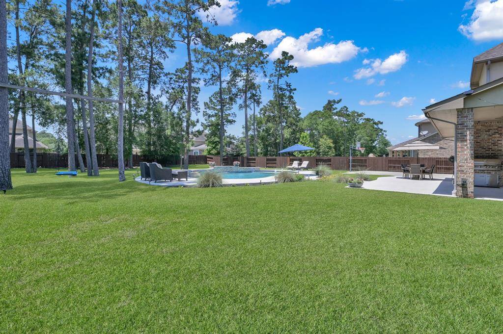 This photo showcases a spacious backyard featuring a well-maintained lawn, a swimming pool with surrounding seating, tall trees providing a natural backdrop, and a covered patio area ideal for outdoor entertaining.