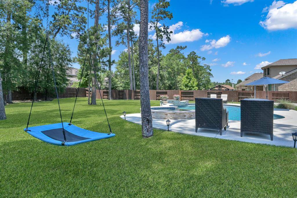 Spacious backyard featuring a lush lawn, tall trees, and a playful swing. The area includes a stylish pool with a spa, surrounded by a patio with comfortable seating, perfect for relaxation and entertaining.