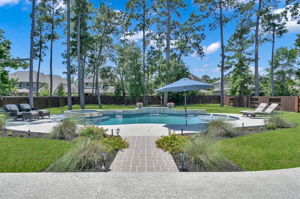 This backyard features a spacious pool surrounded by lush landscaping and tall trees, offering a private retreat. There are plenty of areas for lounge chairs, ready for relaxation, making it perfect for outdoor entertaining.