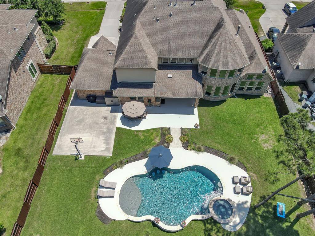 This aerial photo showcases a spacious home with a large backyard featuring a uniquely shaped pool and spa, ample patio space, and a basketball court. It's perfect for outdoor entertaining and family activities.