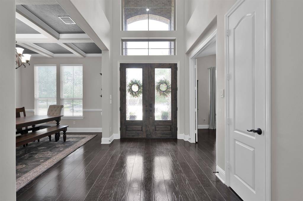 This photo showcases an inviting entryway with elegant double doors. Inside, the space features warm hardwood flooring, neutral walls, and leads to a bright, open living area with a stylish curved staircase.