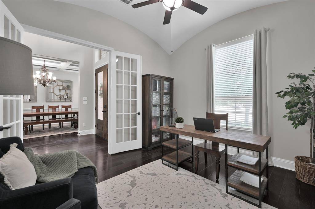 This photo showcases a cozy home office with a large window, allowing plenty of natural light. The room connects to a dining area with elegant French doors, offering a spacious and inviting atmosphere.