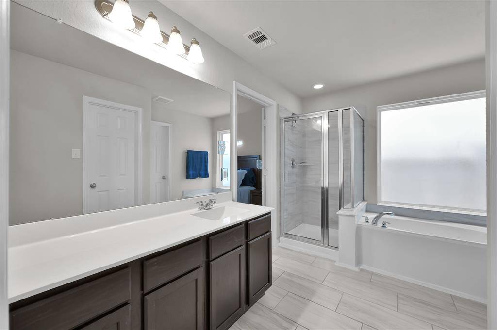This bathroom features a sleek design with a large mirror and a spacious vanity. It includes a glass-enclosed shower and a separate bathtub, all set against a backdrop of neutral tones for a modern and airy feel.