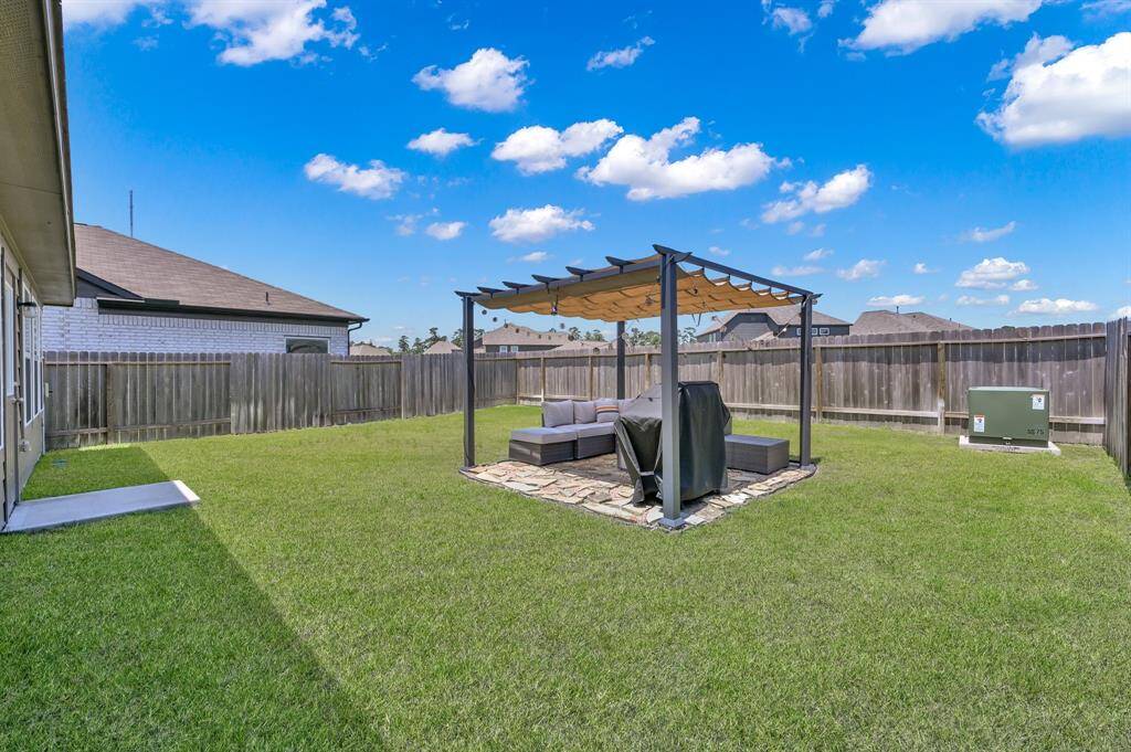 Spacious backyard with a lush lawn, featuring a pergola-covered seating area on a stone patio, perfect for outdoor relaxation and entertaining. The yard is enclosed by a wooden fence, providing privacy and security.