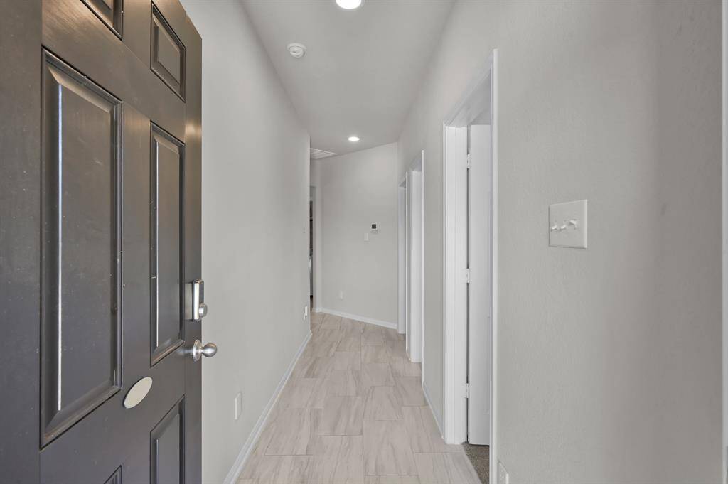 A welcoming entrance hallway with a dark front door, light walls, and wood-like tile flooring. The hallway is well-lit and leads to multiple rooms, offering a clean and modern aesthetic.