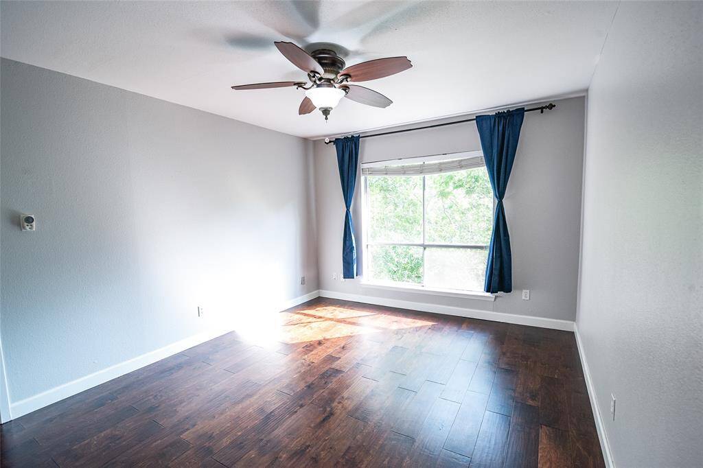 Primary bedroom with ceiling fan, expansive window views of greenery and rich hardwood flooring throughout.