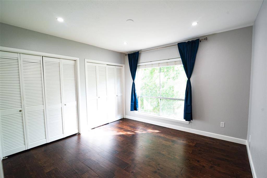 Secondary bedroom. Bright and spacious bedroom featuring large windows with lush green views, ample closet space, and warm hardwood flooring.