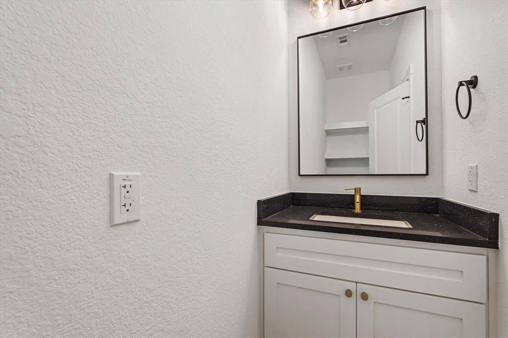 The half bathroom on the first floor includes a black quartz countertop, black & gold fixtures, and built-in shelving above the toilet for décor or linens.