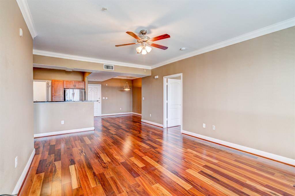 Bright, spacious living room with rich hardwood flooring, ceiling fan, and large arched windows with shutters, offering abundant natural light. Neutral walls and crown molding add elegance, with open doorways leading to adjacent rooms.