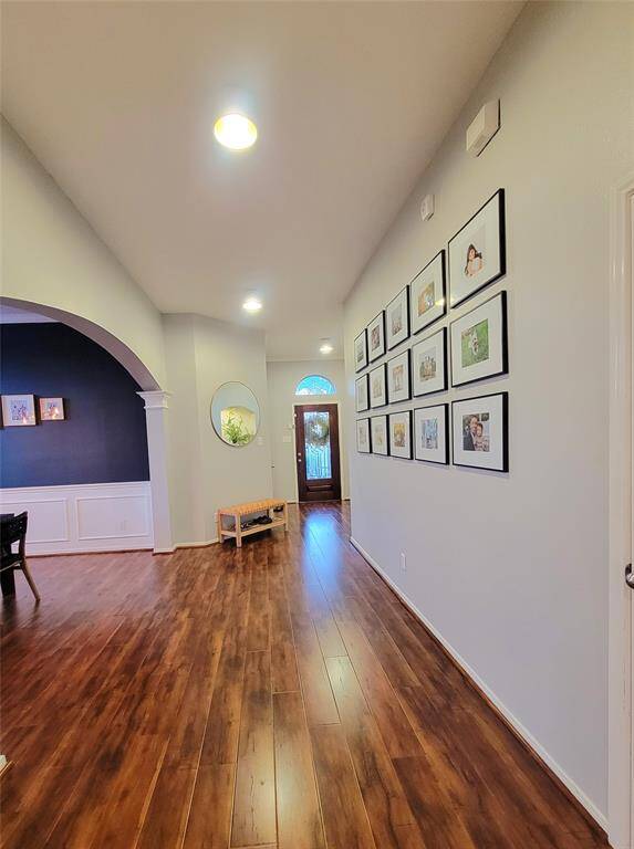 Bright and welcoming entryway with wood flooring, recessed lighting, and a gallery wall. The archway leads to a dining area with wainscoting and a dark accent wall. A glass-paneled front door adds elegance.