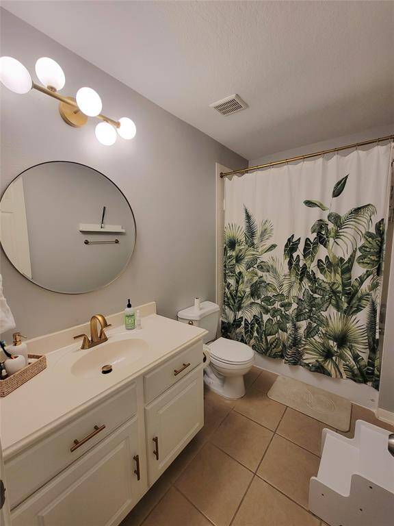 This bathroom features a modern design with a round mirror, stylish light fixtures, and a vanity with a light countertop and gold fixtures.