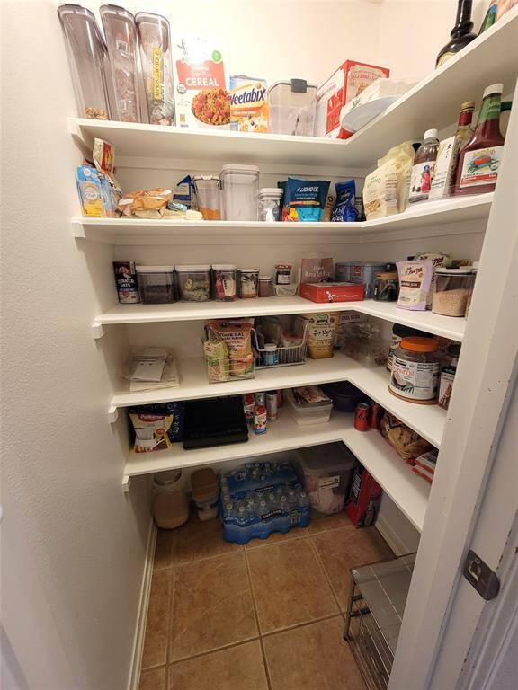 This photo shows a well-organized pantry with several white shelves stocked with various food items and kitchen supplies. The space is bright and neatly arranged, offering ample storage for household essentials.