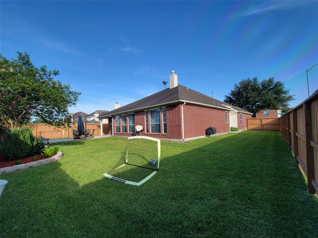 Spacious backyard with well-maintained lawn and patio area, perfect for outdoor activities and relaxation, bordered by a wooden fence for privacy.