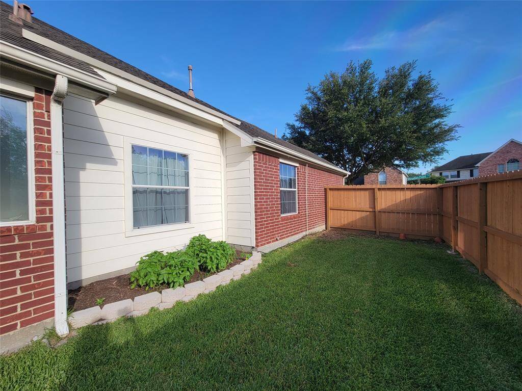 This photo shows a cozy backyard with a well-maintained lawn, bordered by a wooden fence. The exterior features a combination of red brick and white siding, with a small garden bed under the window. It's a private, inviting outdoor space.