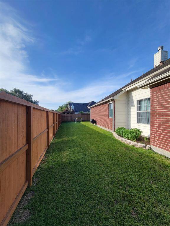 This photo showcases a side yard with a well-maintained lawn, bordered by a wooden fence on one side and a brick house on the other. The space is open and bright, ideal for outdoor activities or gardening.