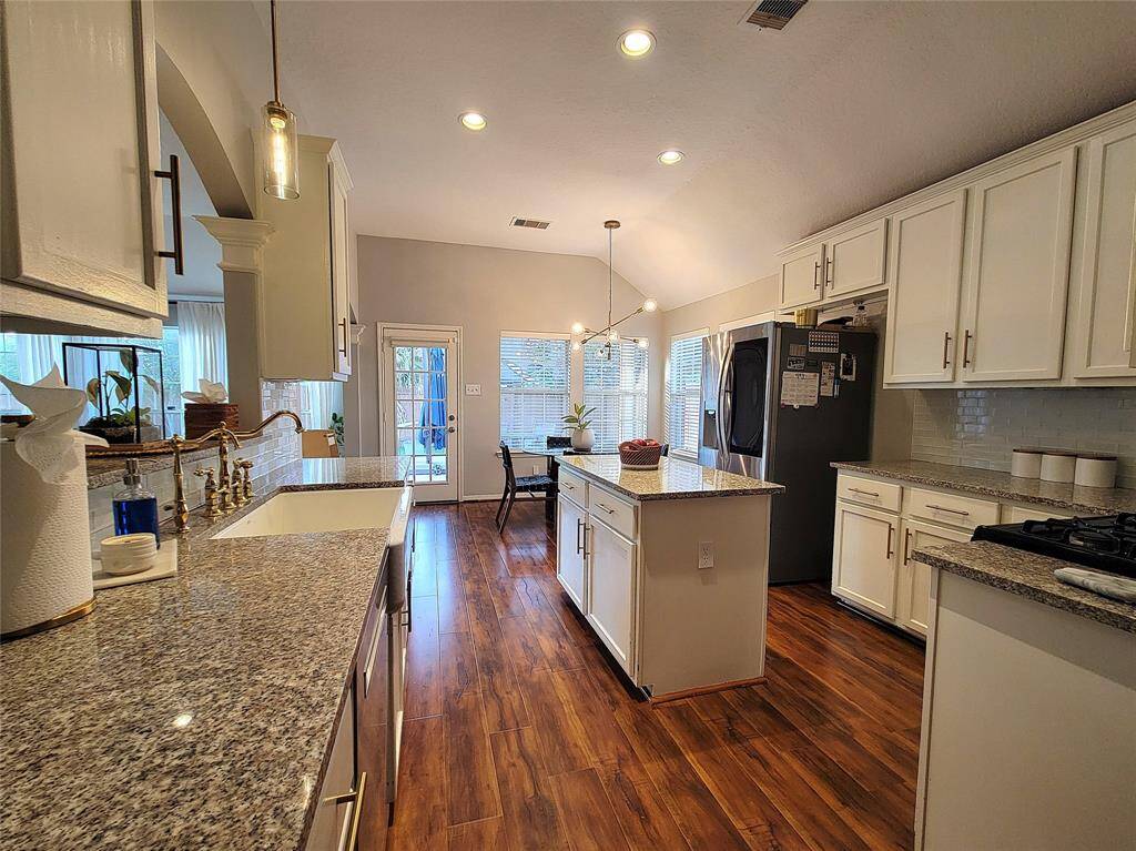 This kitchen features modern granite countertops, a central island, and ample cabinetry. The wood flooring adds warmth, and large windows provide natural light. Stainless steel appliances complete the contemporary look.