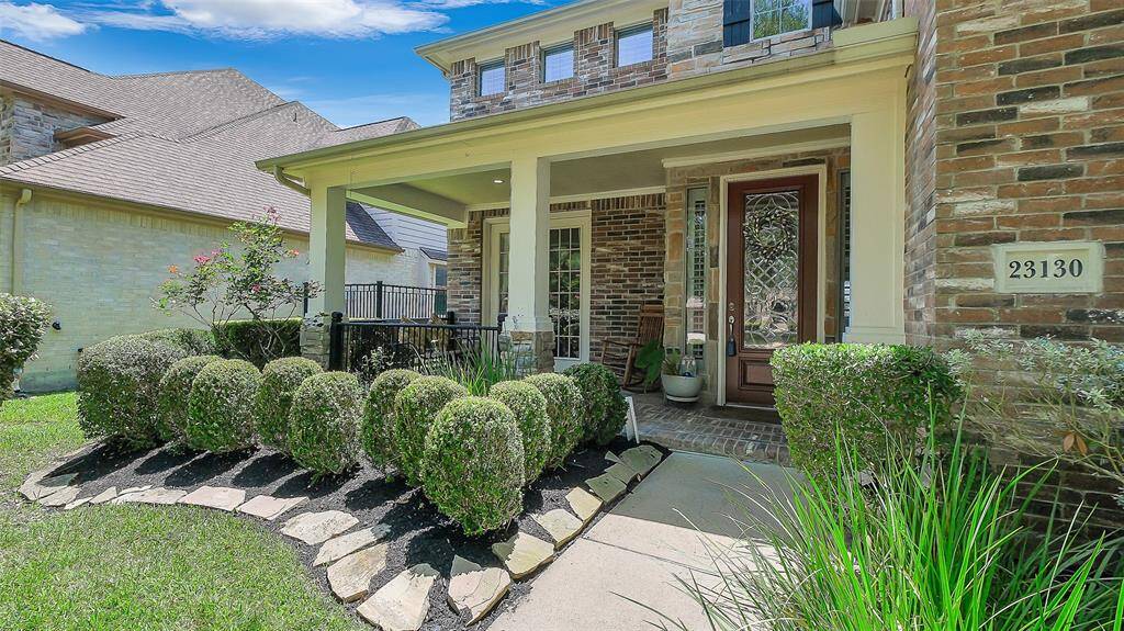 Covered front porch entryway with leaded glass front door and French doors opening to the formal dining room. Manicured landscaping.