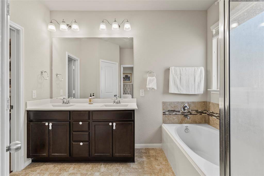 Every morning starts right here—natural light streaming through the frosted window as you stand at the double vanity, coffee still in hand. The oversized mirror gives you plenty of space to get ready without bumping elbows, and when the day winds down, the soaking tub is always waiting. This space feels calm, clean, and just indulgent enough.
