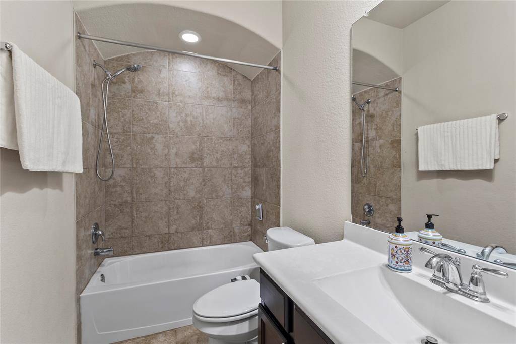 Guests feel right at home in this full bath, featuring a tiled shower with arched detailing, a wide vanity for added space, and soft lighting that keeps the atmosphere fresh and welcoming.